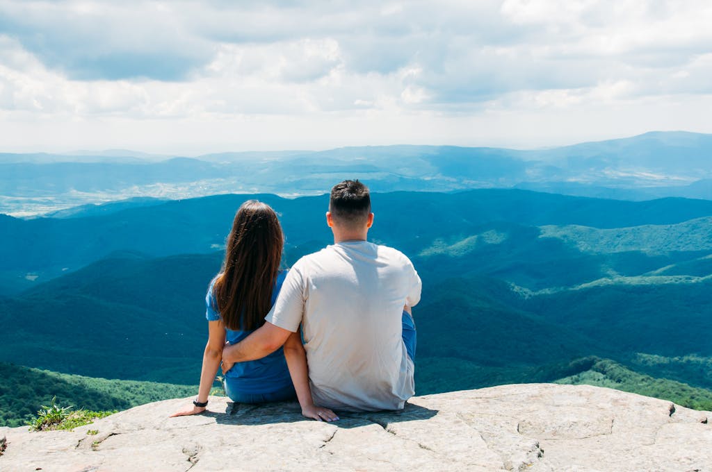 A couple sitting on a rock overlooking the mountains