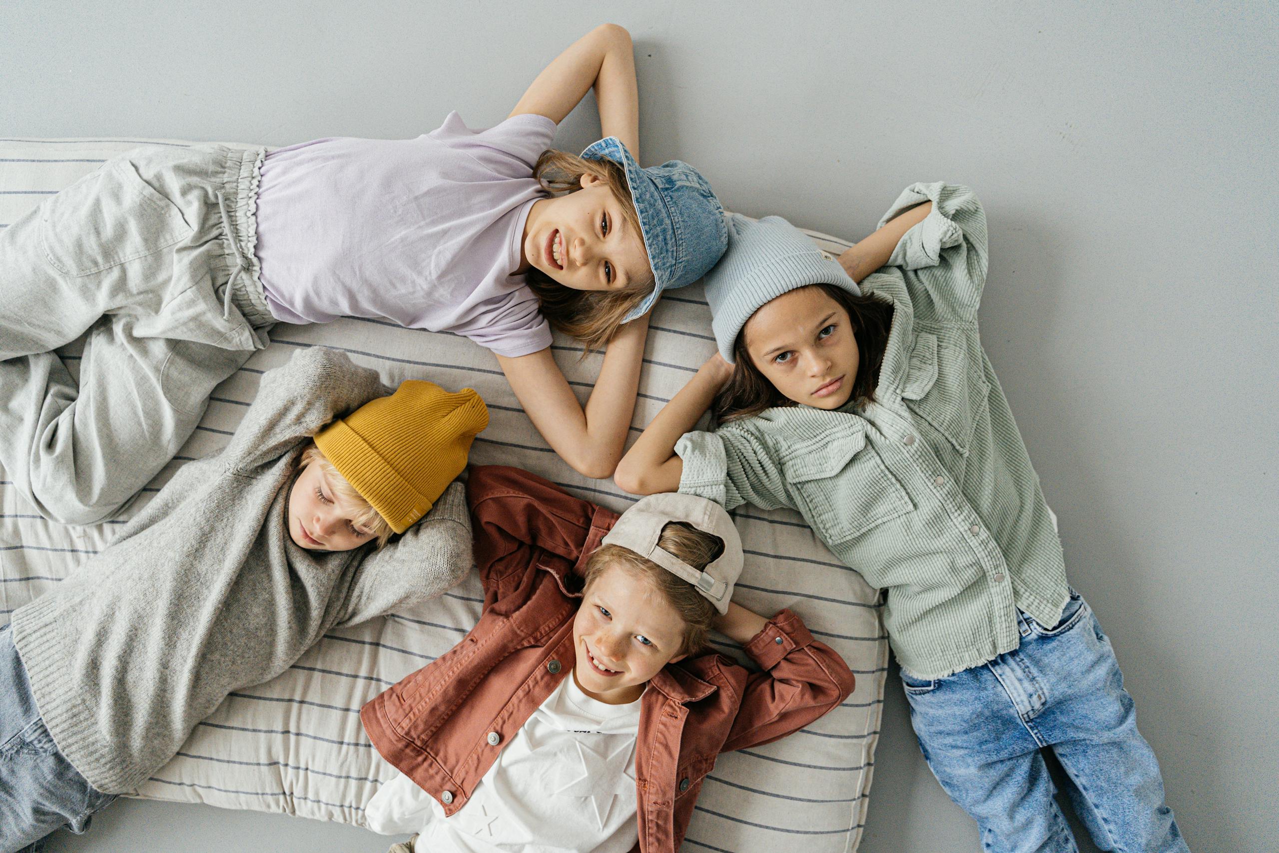 Four children in casual attire lying on a cushioned surface, relaxed and playful.